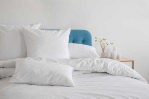 White pillows, duvet and duvet case on a blue bed. White bed linen on a blue sofa. Bedroom with bed and bedding. Messy bed. Front view.
