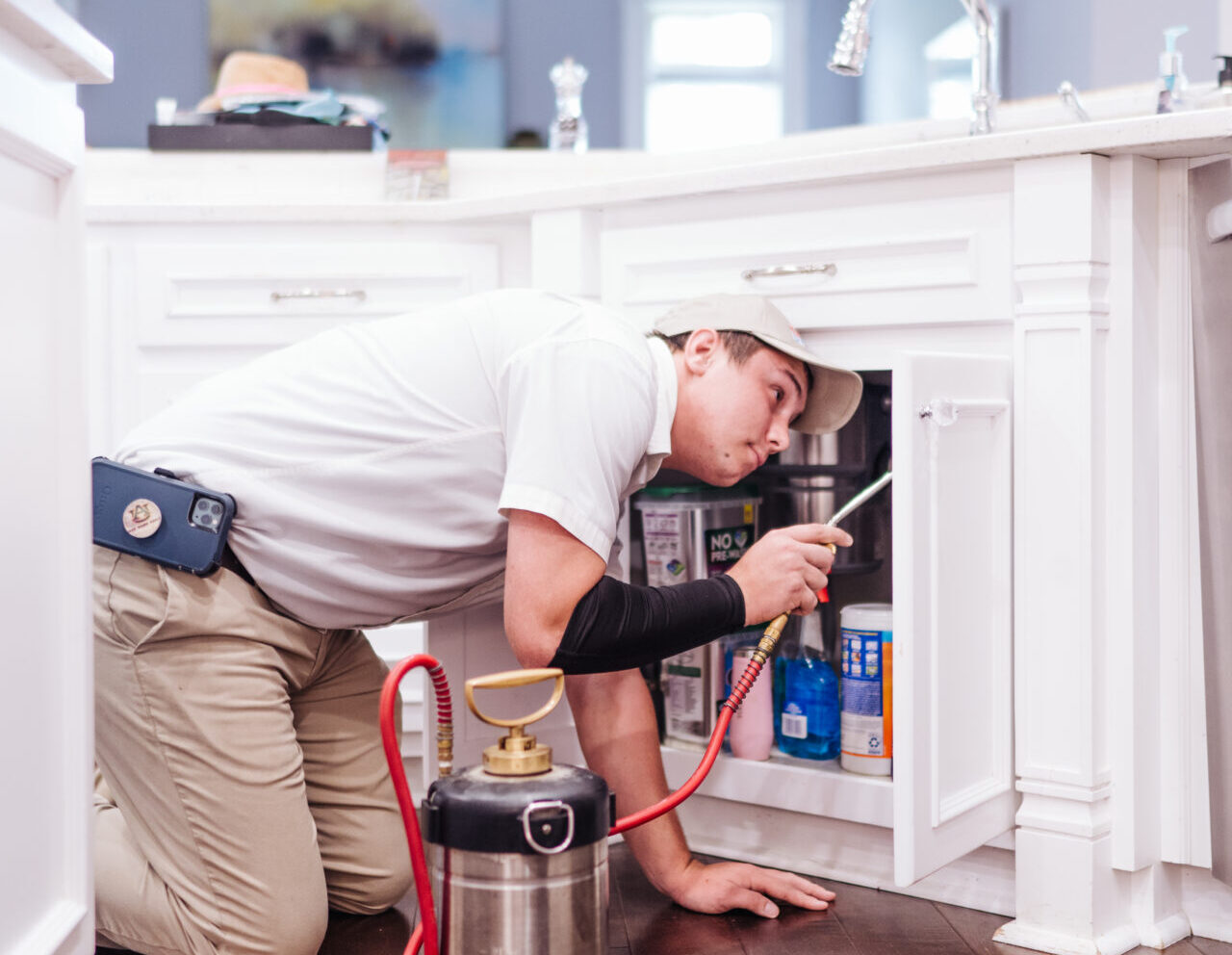 man spraying for pests under a kitchen counter